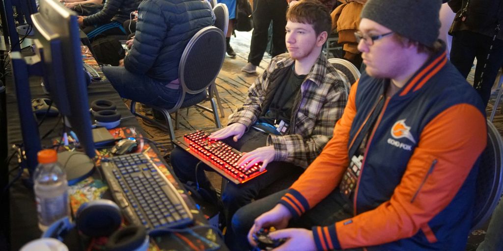 man using video game control pad beside man using computer keyboard sitting and playing video games