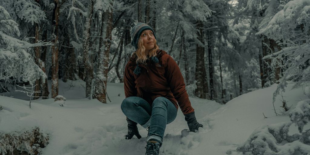woman in brown jacket and blue denim jeans sitting on snow covered ground