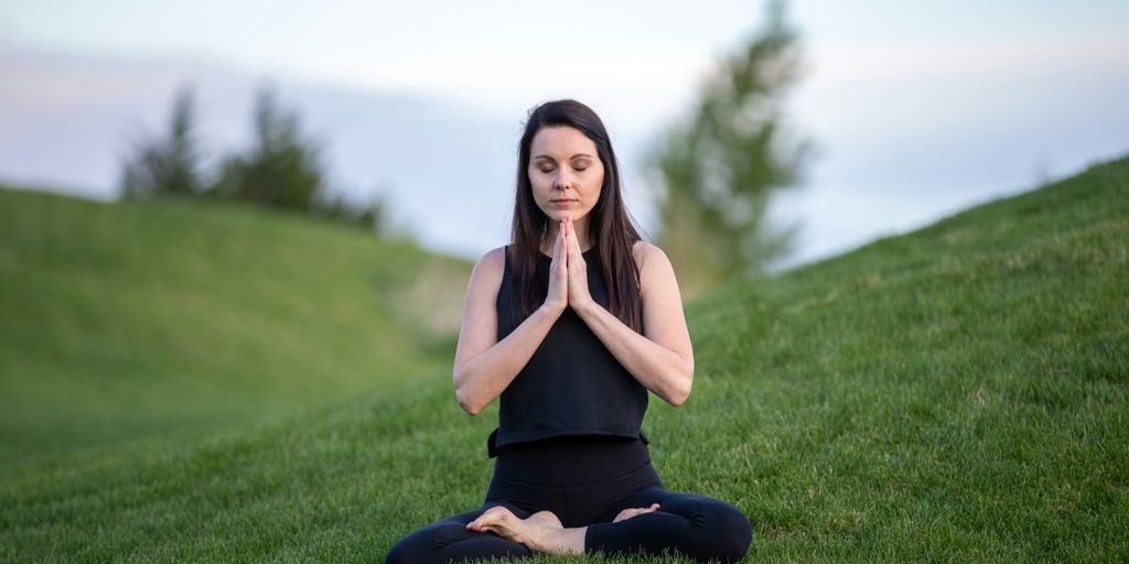 woman in black tank top and black pants sitting on green grass field during daytime