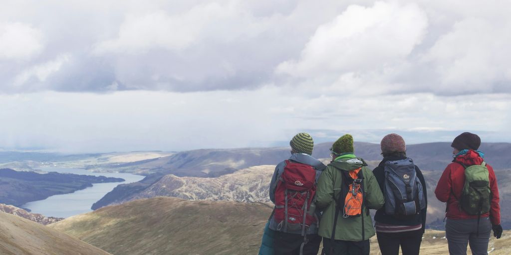 four person standing while looking on mountain view with body of water at daytime