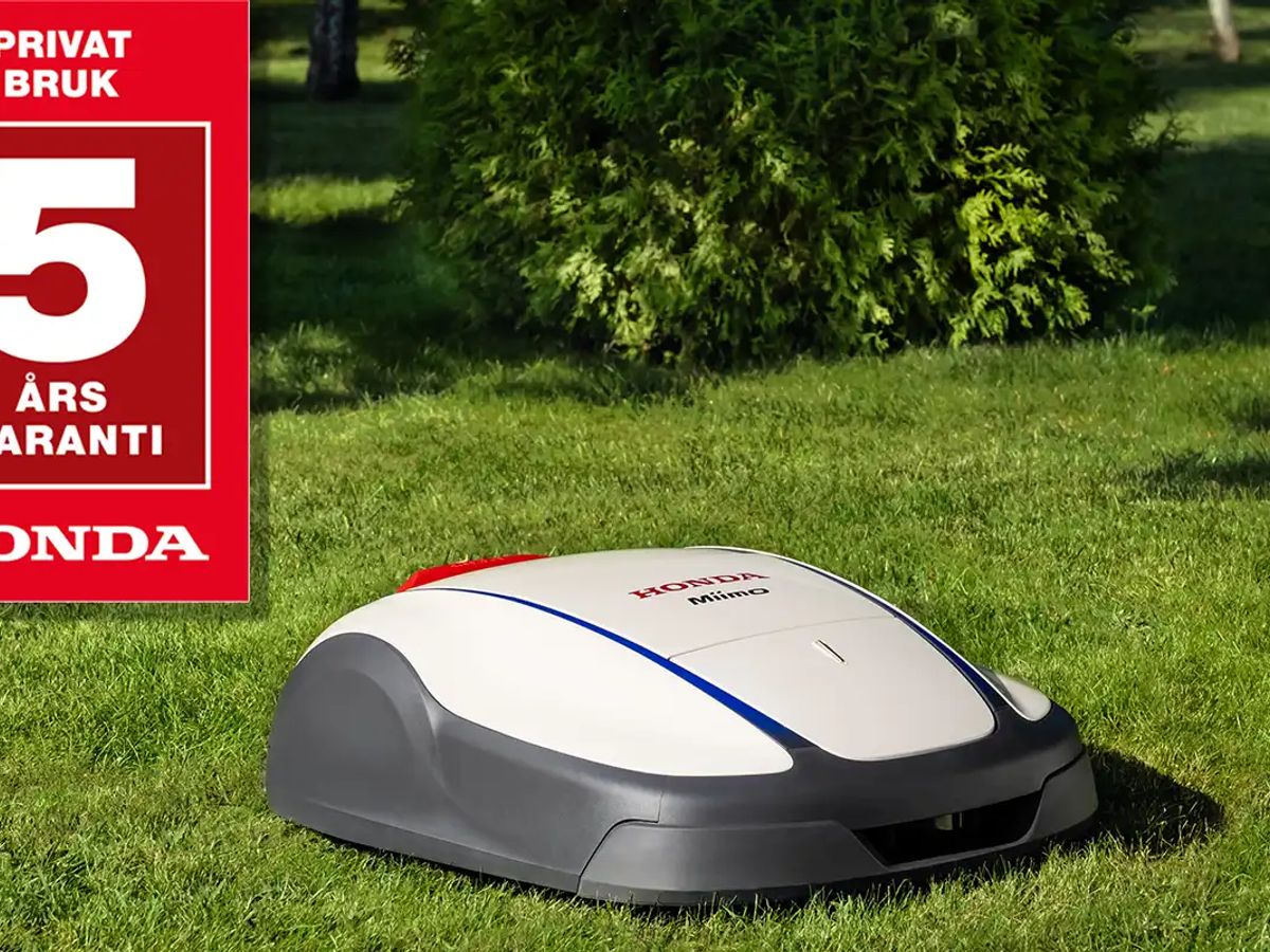 A robotic mower on green grass, featuring a warranty sign.