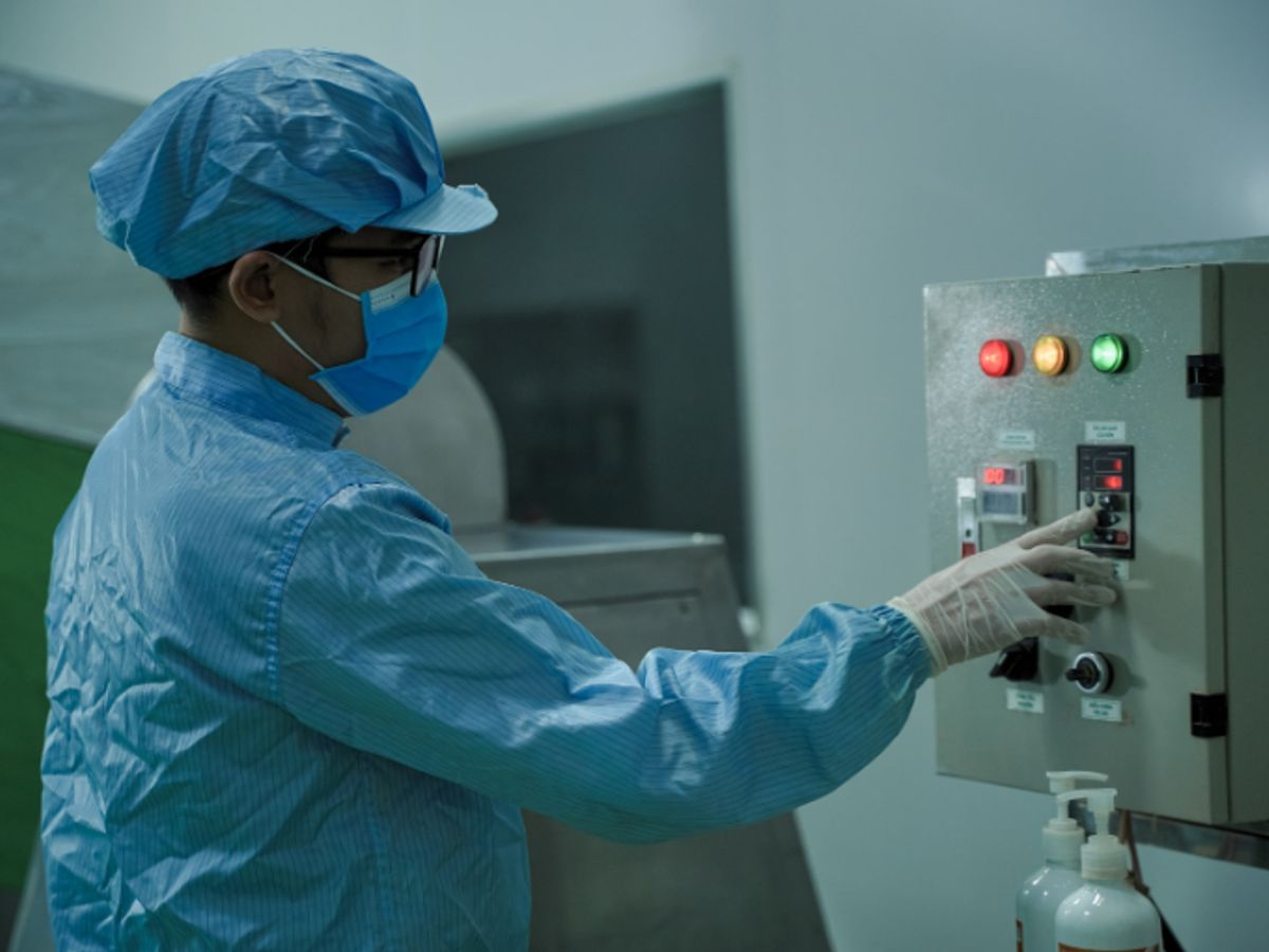 Person in protective gear operating machinery in a sterile environment.