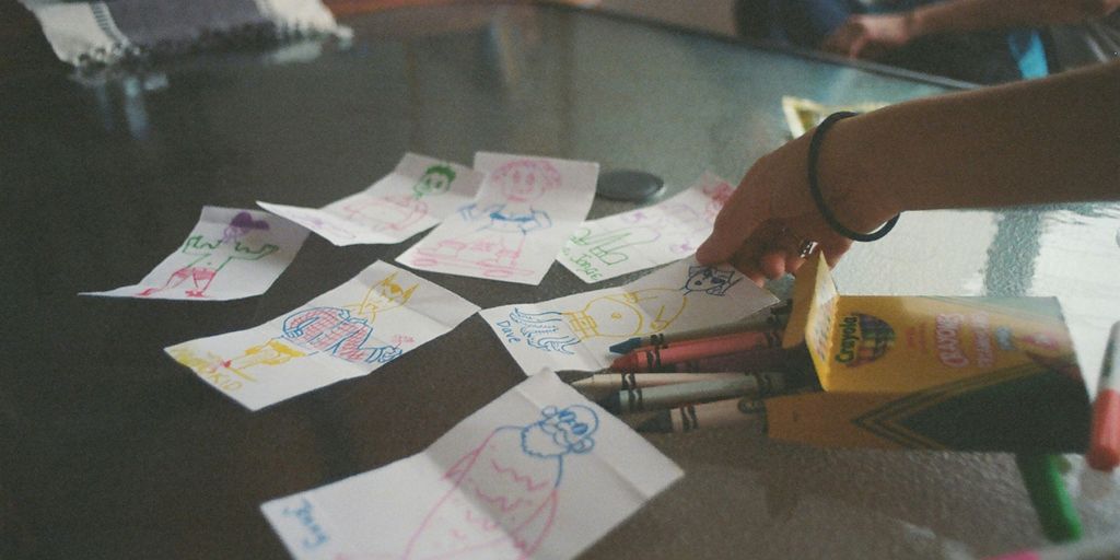 a child's hand writing on paper with crayons