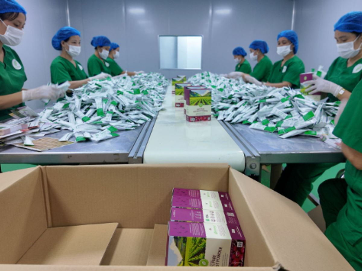 Workers in green uniforms packaging products in a warehouse.