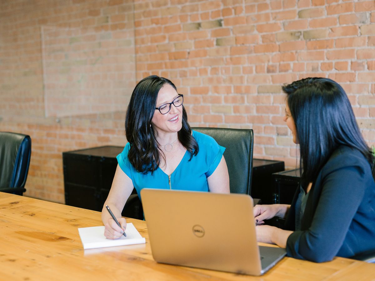 woman in teal t-shirt sitting beside woman in suit jacket