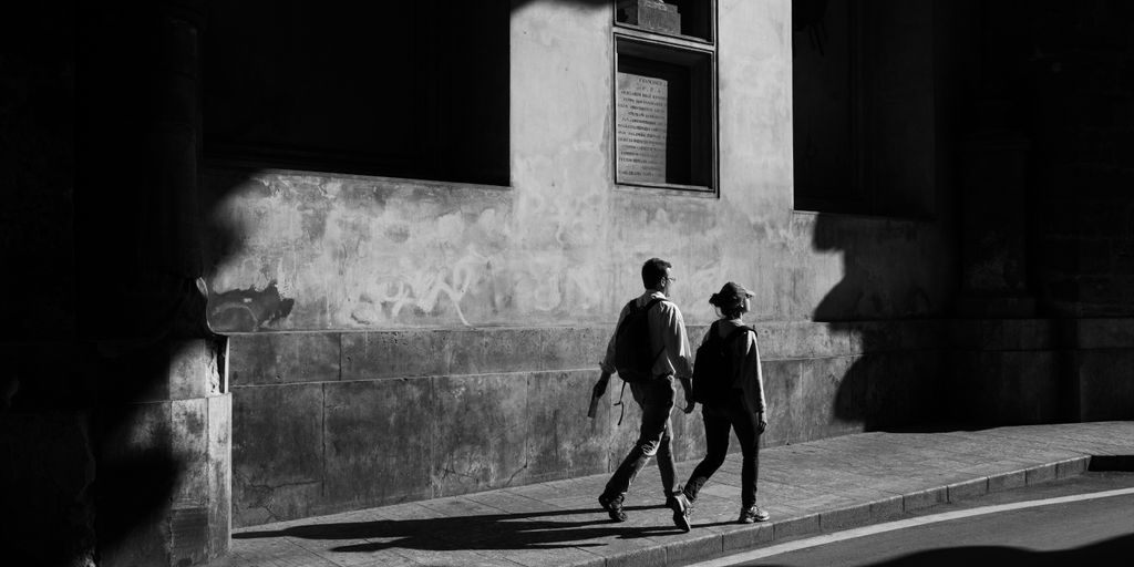 gray scale photo of man and walking near concrete building