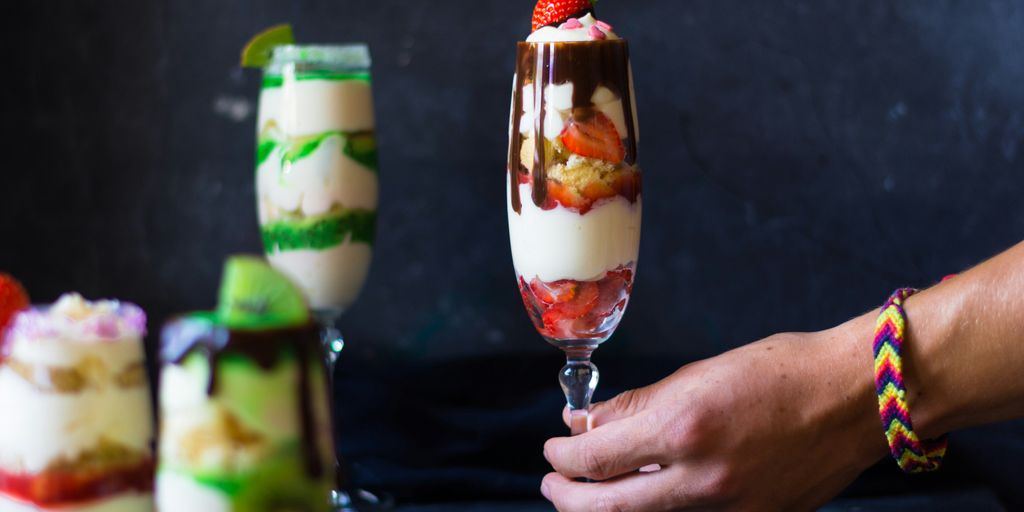 person holding clear glass footed cup with strawberry and cream