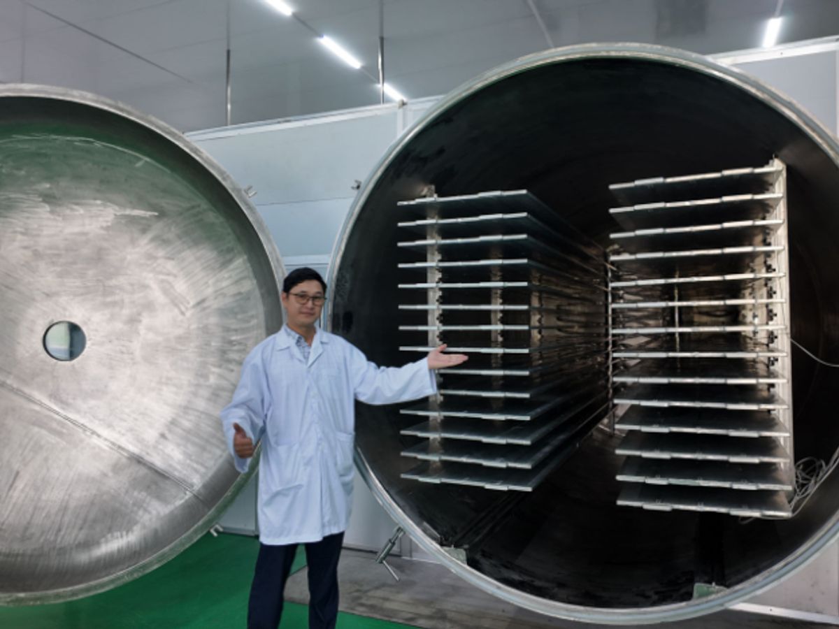 A person stands beside a large industrial vacuum chamber.