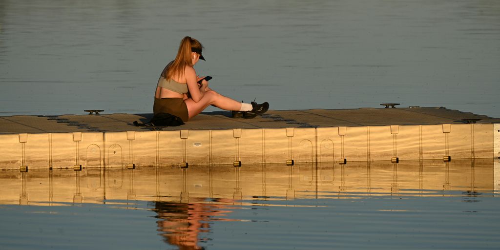 Woman sitting and looking at her phone by the water.