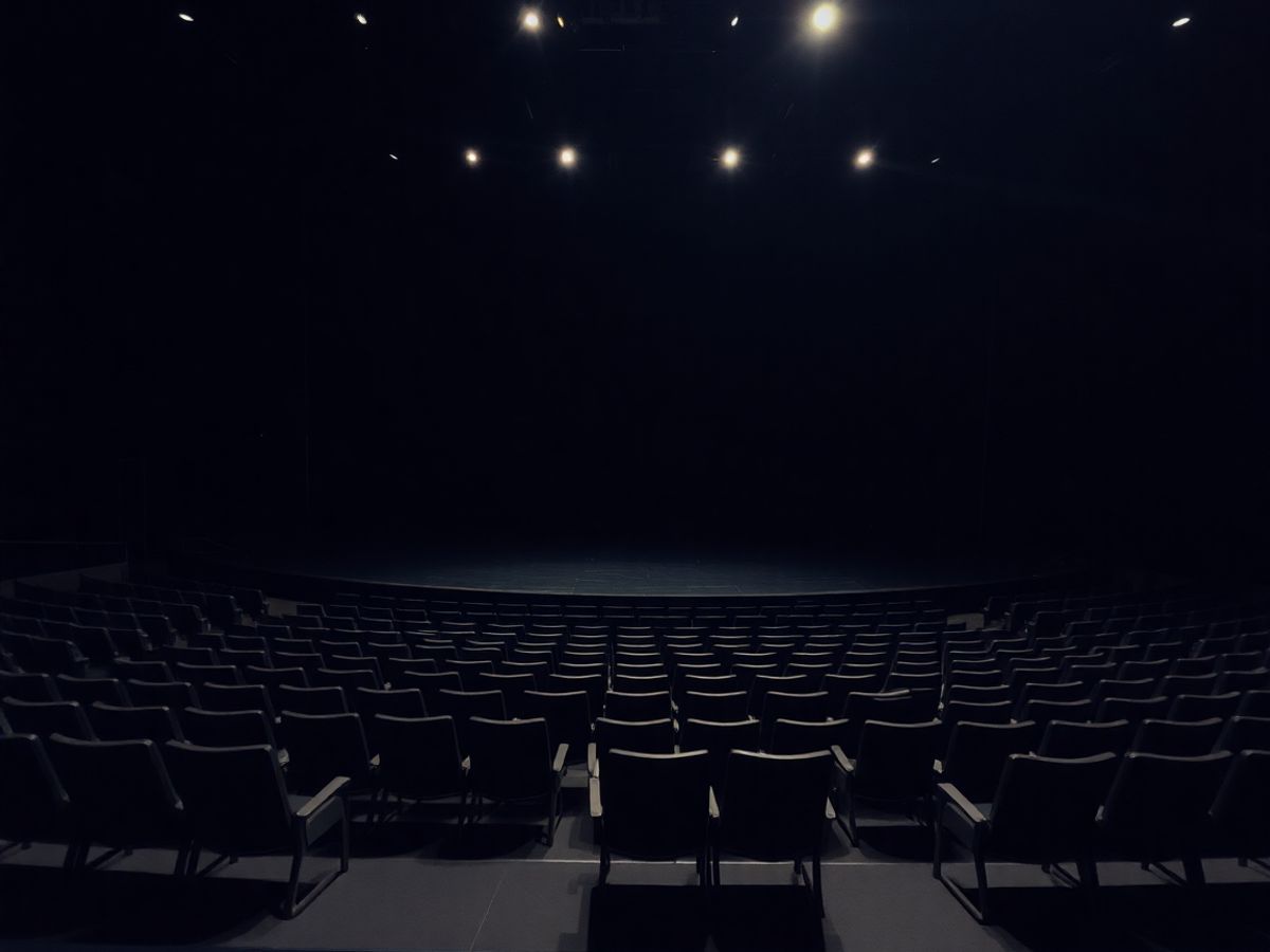 O scenă de teatru goală, cu lumini slabe și scaune goale.