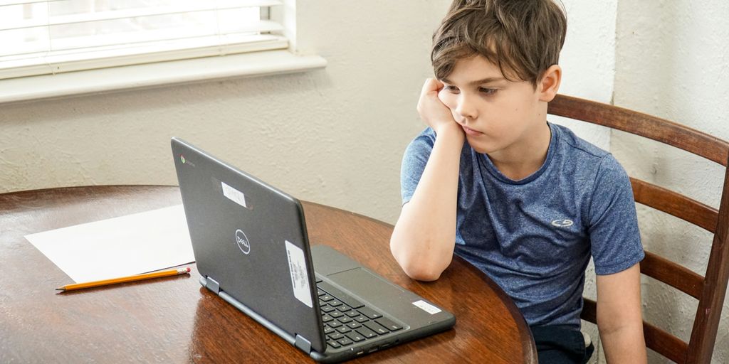 boy in blue crew neck t-shirt using macbook pro on brown wooden table