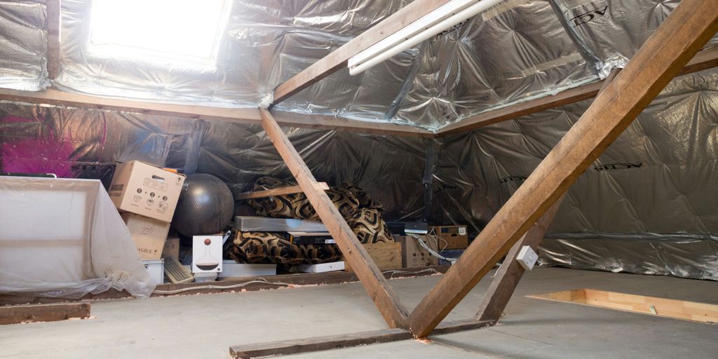 A dusty attic with insulation and wooden beams.
