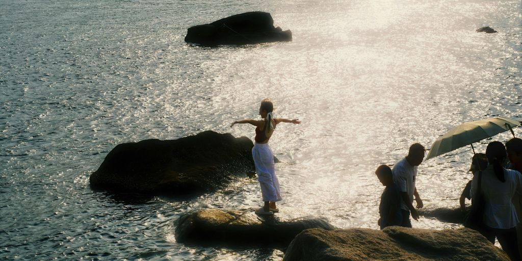 A person balances on a rock near the ocean.