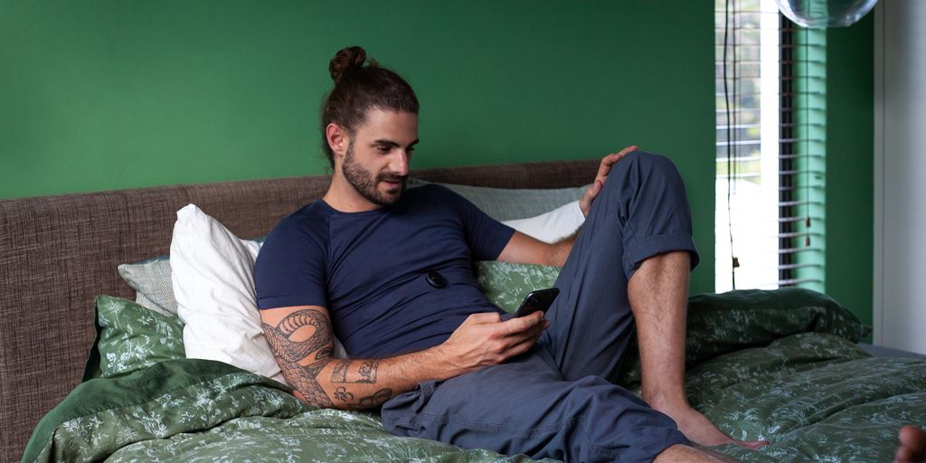a man sitting on a bed looking at his cell phone