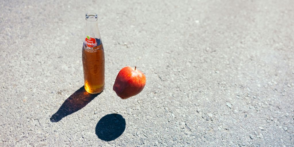 a bottle of soda and an apple on the ground