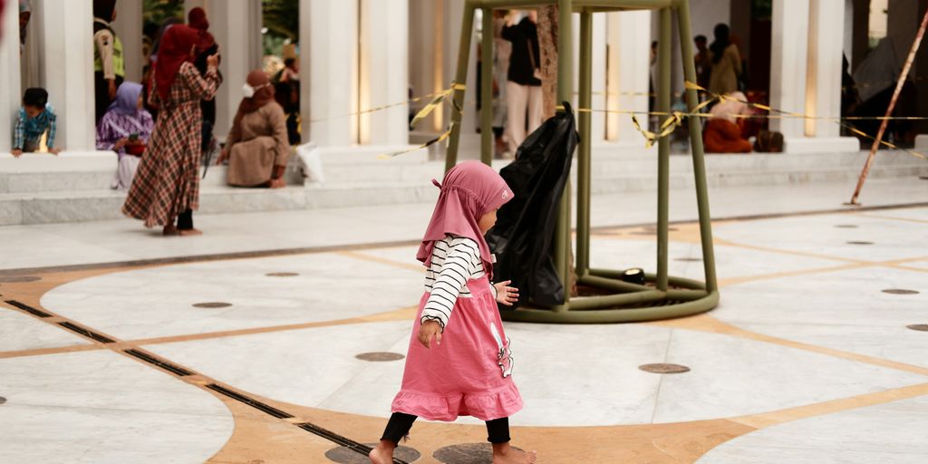 a little girl in a pink hijab walking through a building