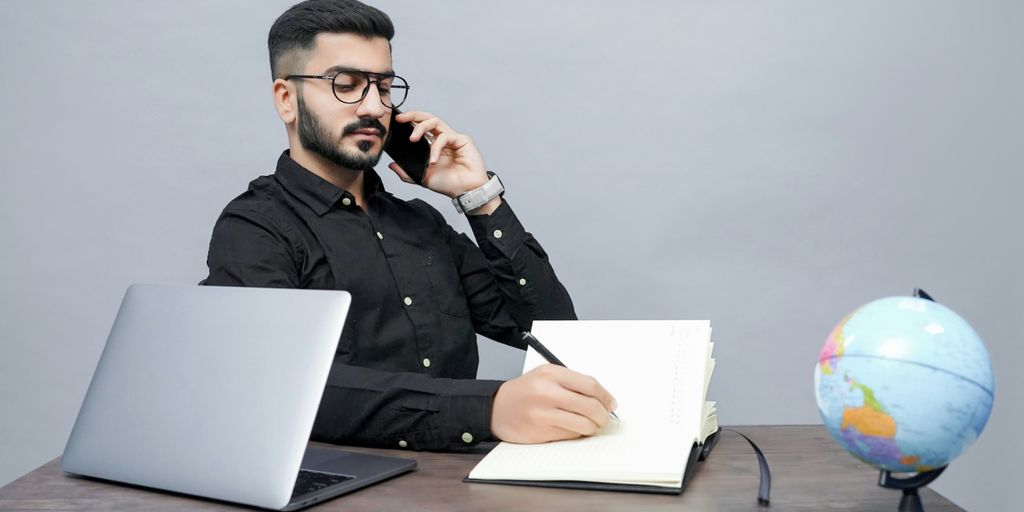 a man holding a pen and a book and a laptop