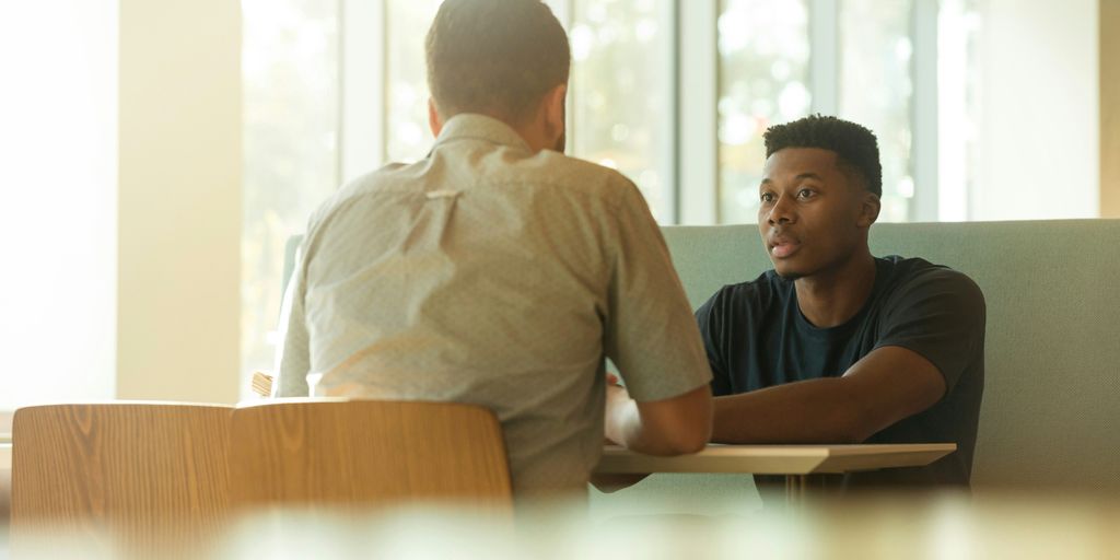 Two individuals engaged in a serious conversation at a table in a bright, modern setting, emphasizing client interactions and collaboration in financial services.