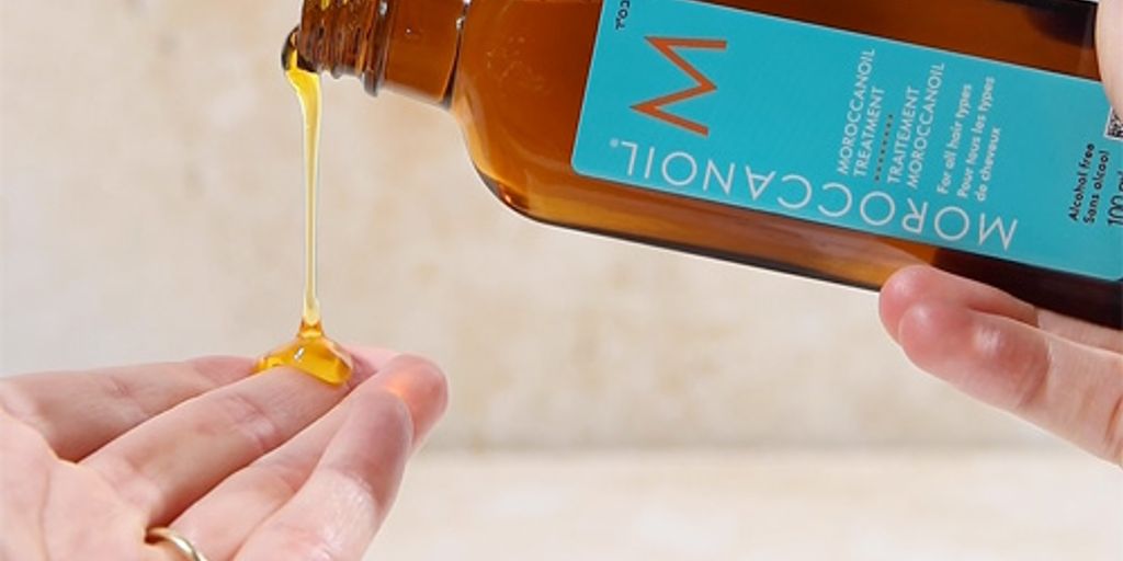 Bottle tilted, pouring golden liquid onto a hand, skincare product.
