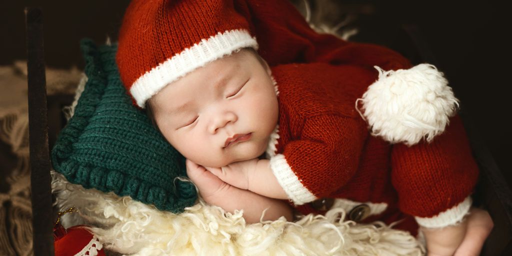 A baby wearing a santa hat sleeping on top of a stuffed animal