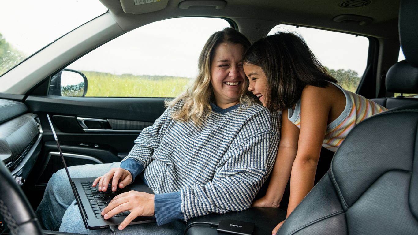 Woman works on laptop with child in car.