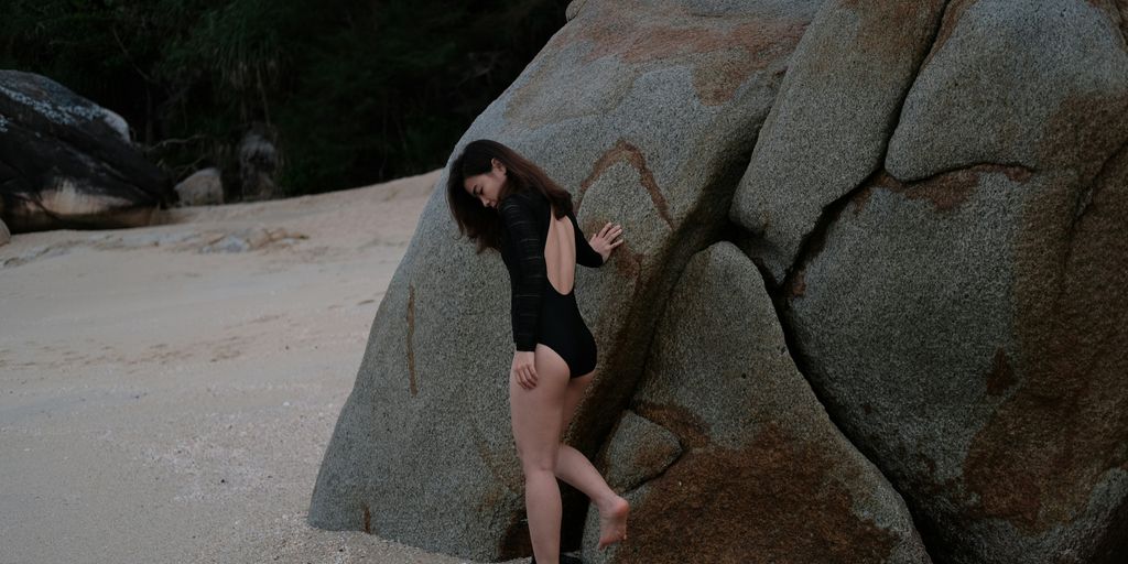 a woman in a bathing suit standing next to a large rock