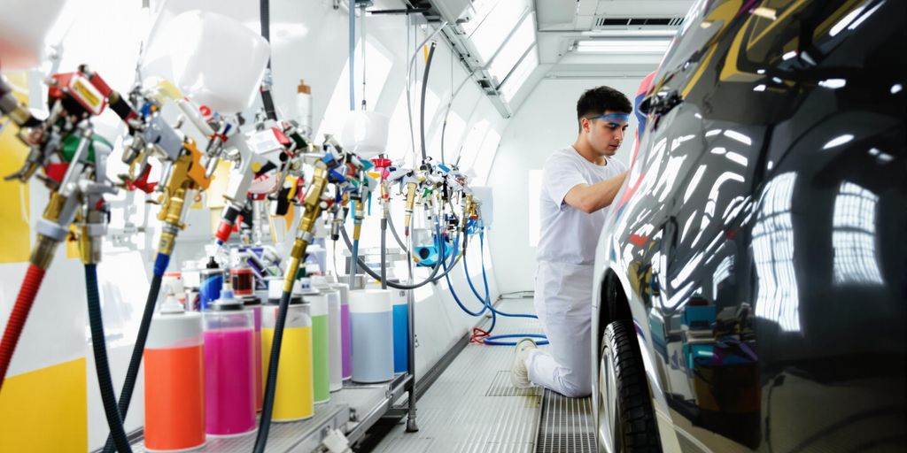 Technician painting a car in a colorful paint booth.