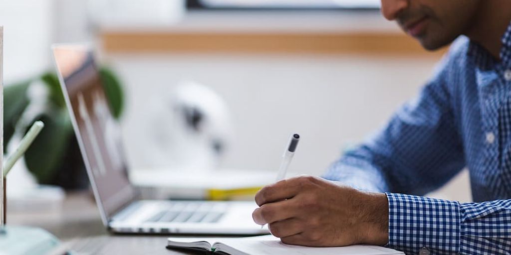 person writing on a laptop with AI assistant, books and notes around, modern office setting