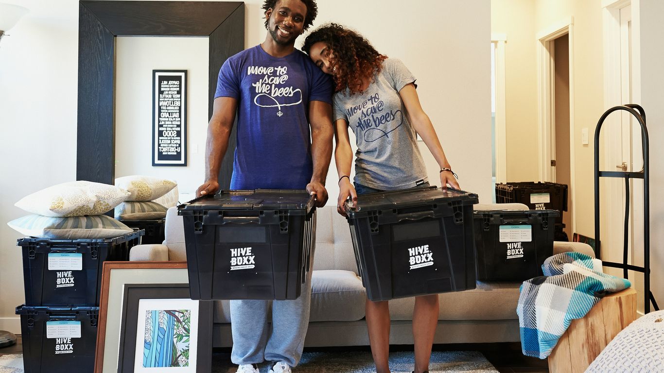 woman in blue tank top and gray leggings holding black suitcase