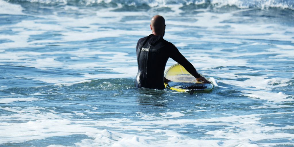 man in black wet suit holding yellow surfboard on sea during daytime