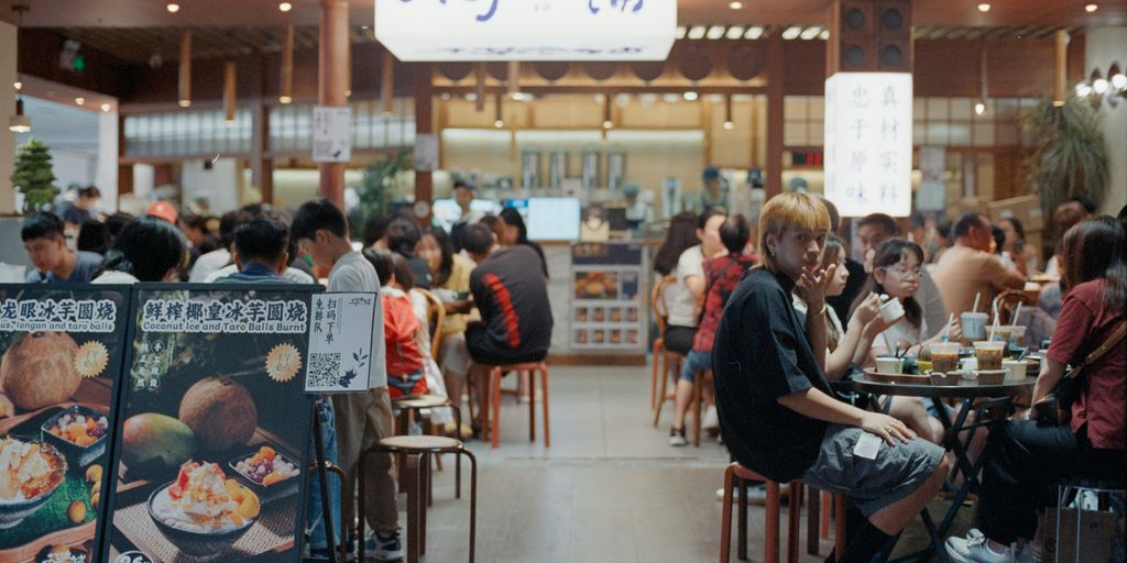 People eating at a busy food court with signs.