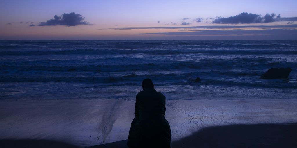 silhouette of person sitting on seashore during sunset