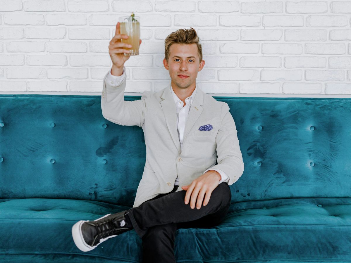 man in gray blazer raising drinking glass while sitting on sofa