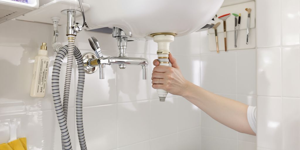Person fixing a leaky pipe under a sink.