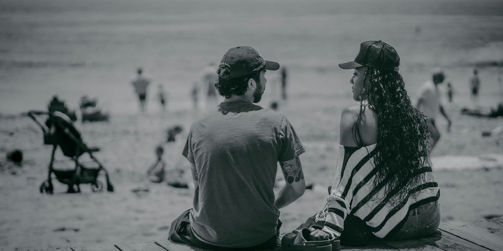 a man and a woman sitting on a pier looking at the beach