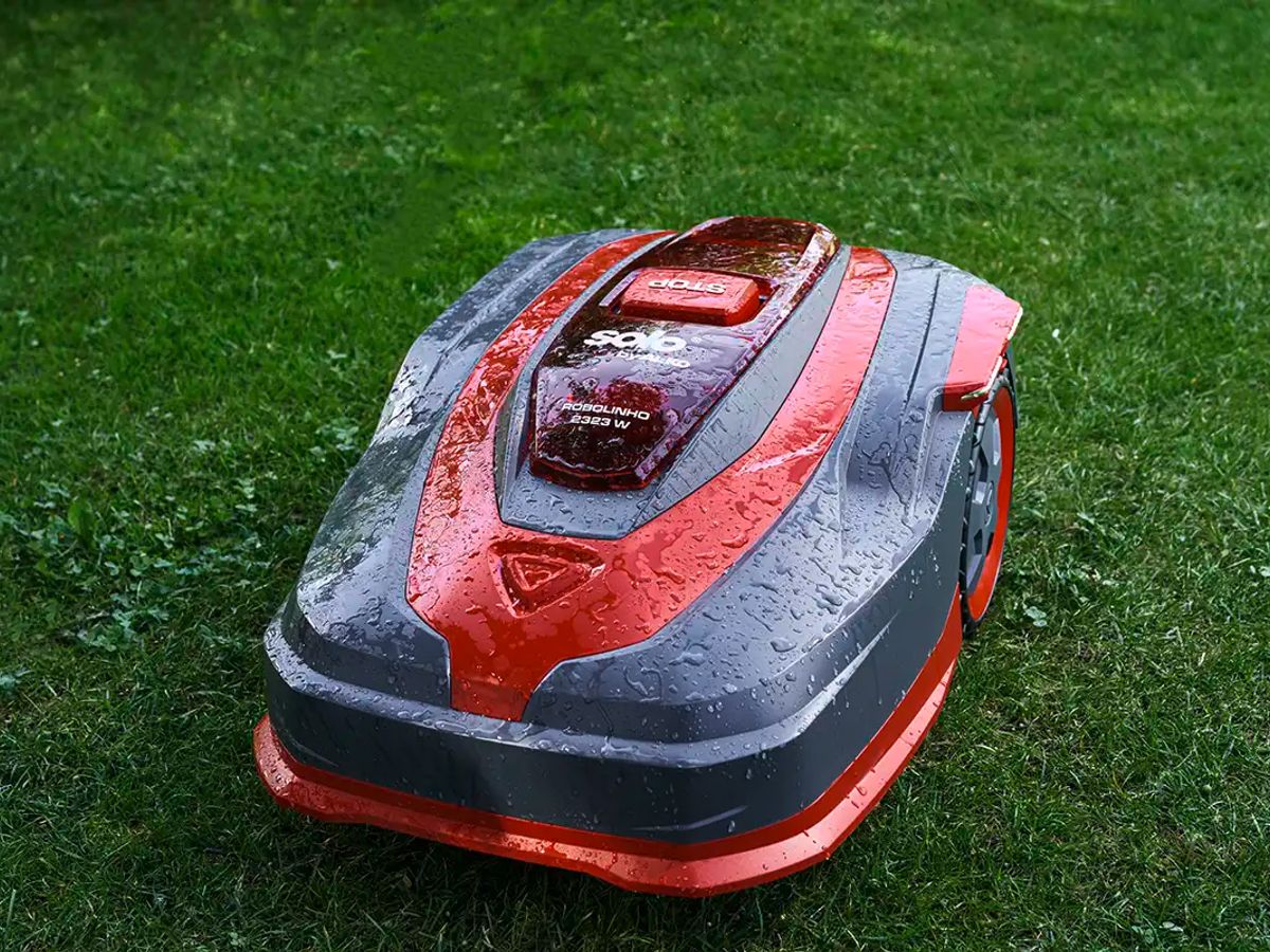 Robot lawn mower on wet grass in a garden setting.