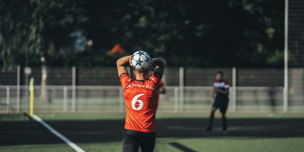 man in orange jersey shirt and black shorts playing soccer during daytime