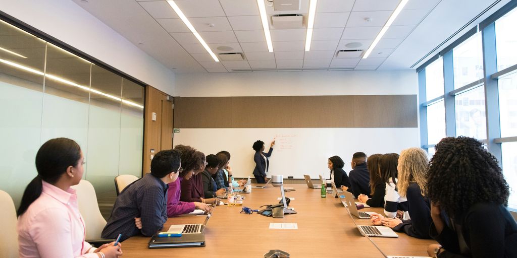 people on conference table looking at talking woman