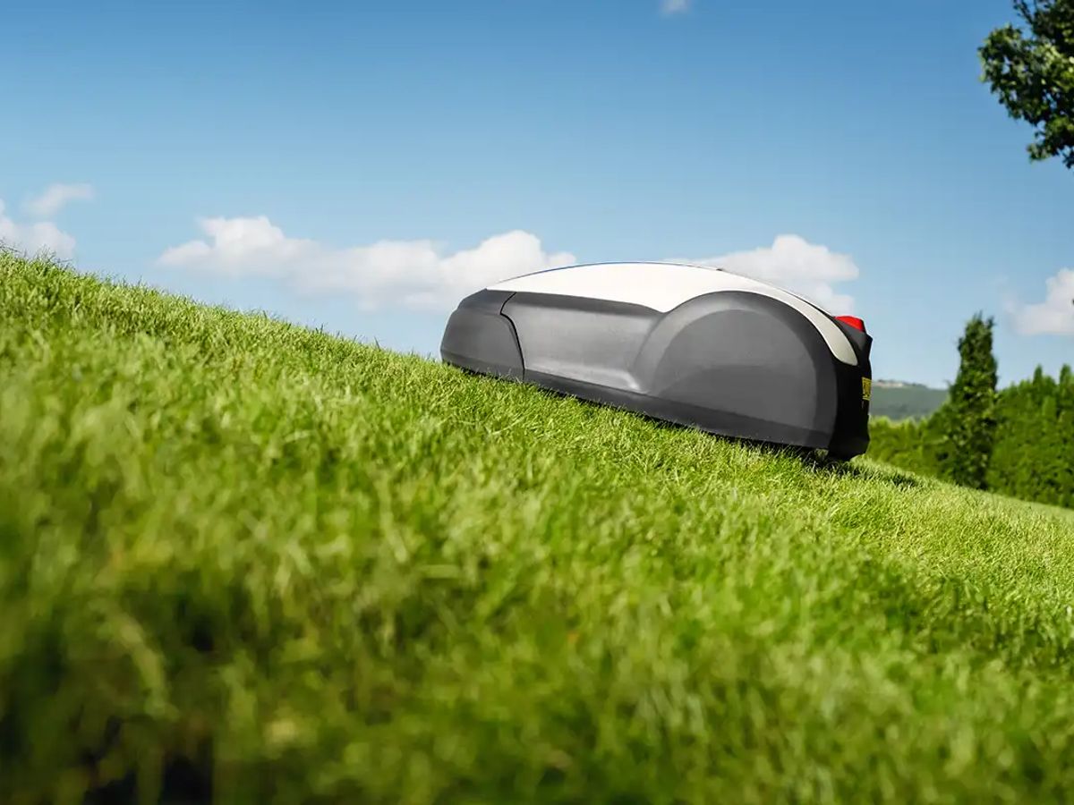 A robotic mower navigating a grassy hillside under a blue sky.