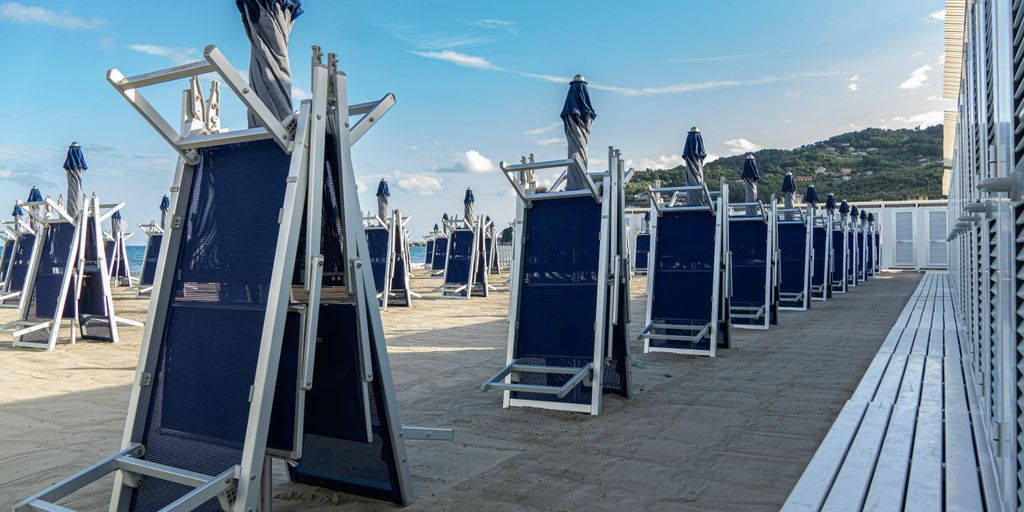 a row of blue chairs sitting on top of a sandy beach