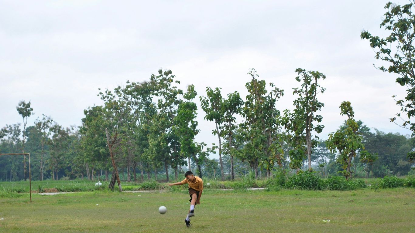 boy in brown shirt playing soccer on green grass field during daytime