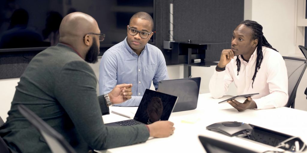 a group of people sitting around a table with laptops