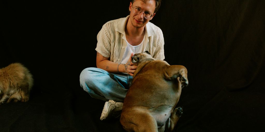 Man smiles while petting a dog on black background.
