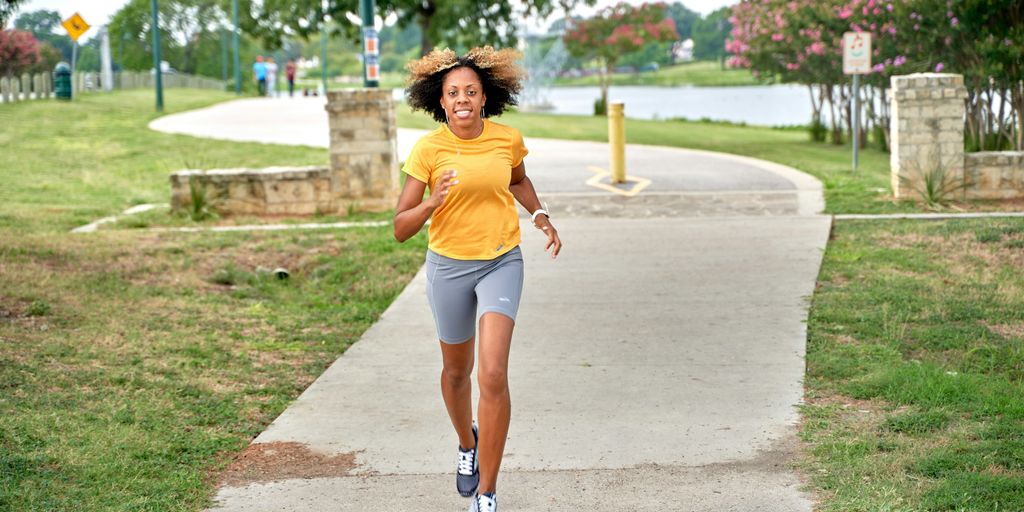 a woman running down a sidewalk in a park
