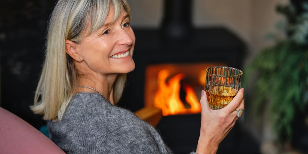 a woman holding a glass of wine in front of a fireplace