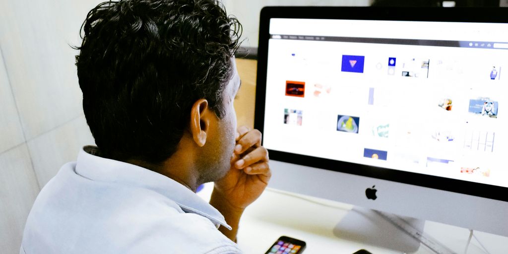 man sitting in front of silver Apple iMac on table