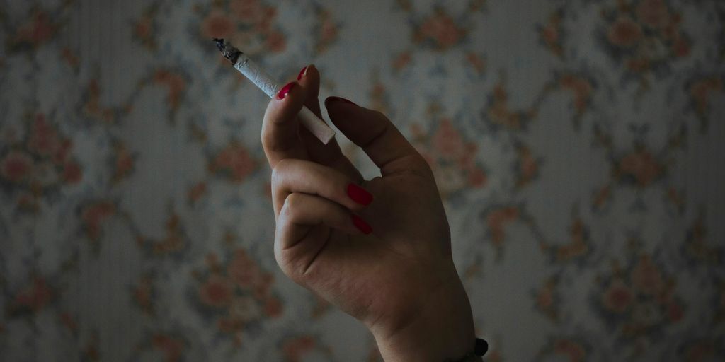 person holding cigarette stick in front of white and pink floral textile