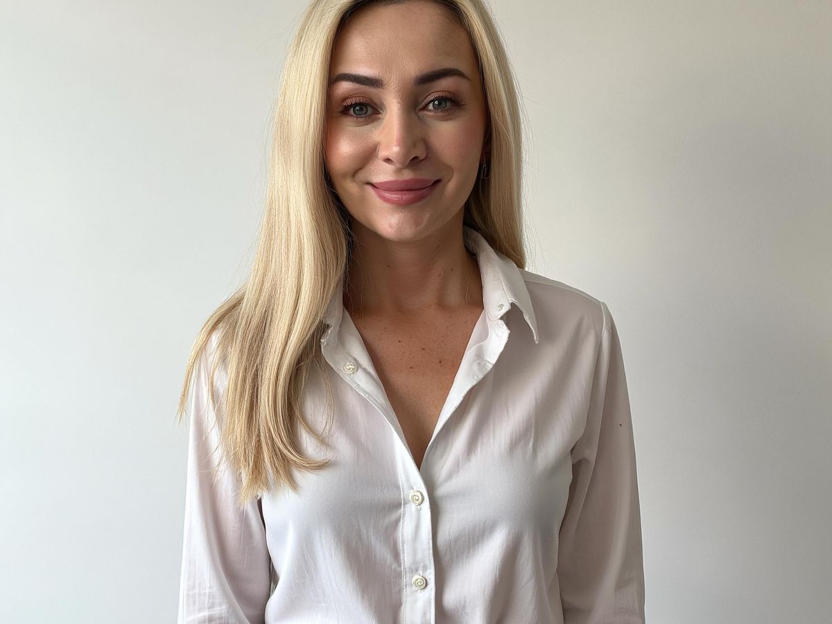 A woman in a white shirt smiles against a plain background.