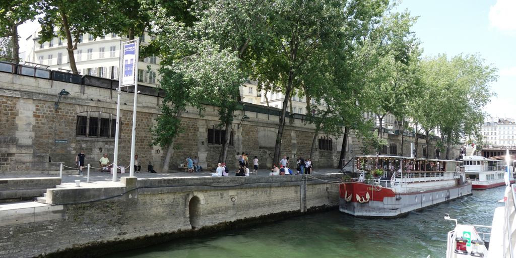 Boats sail on a river near a stone wall.