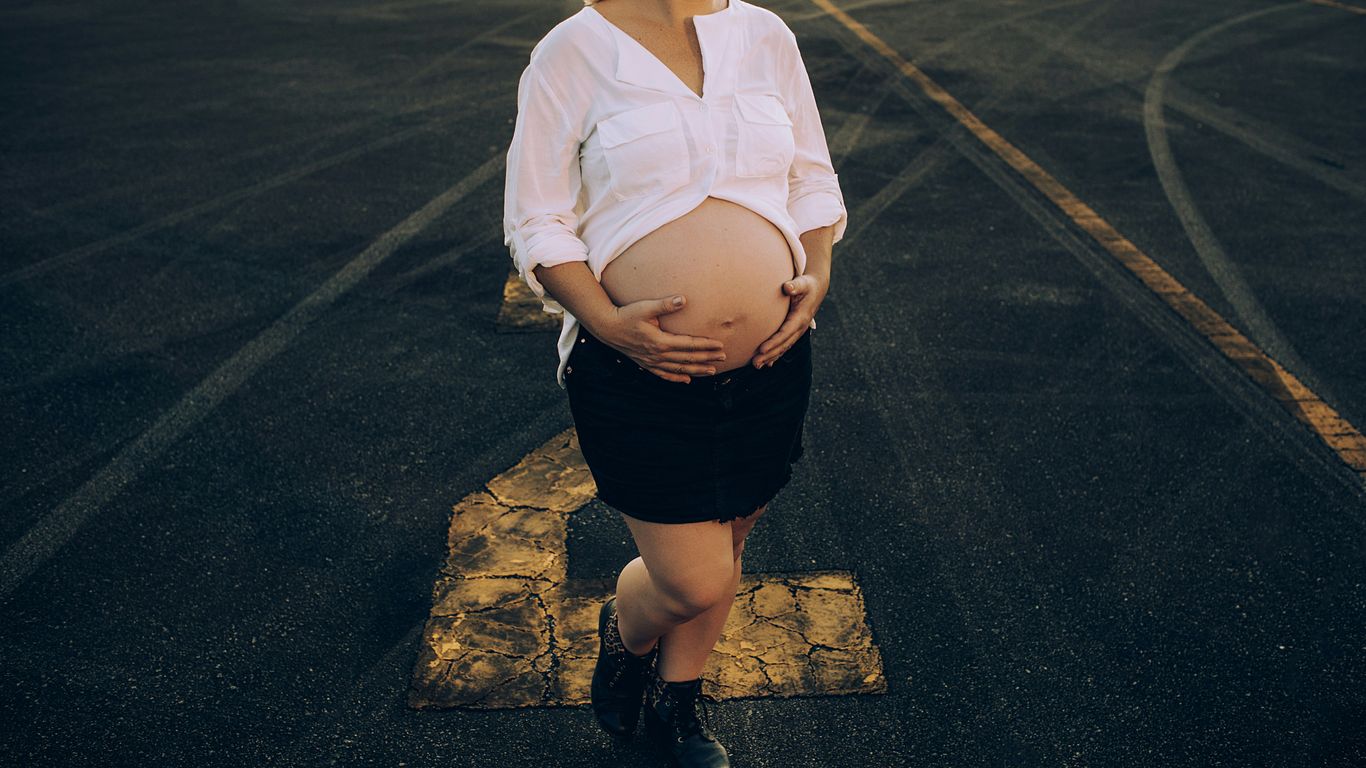 woman in white dress shirt and black skirt standing on gray asphalt road during daytime